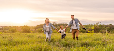 Happy family in the park evening light. The lights of a sun. Mom, dad and baby happy walk at sunset. The concept of a happy familyの写真素材