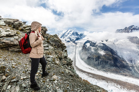 Young happy woman with backpack standing on a rock and looking to a valley below