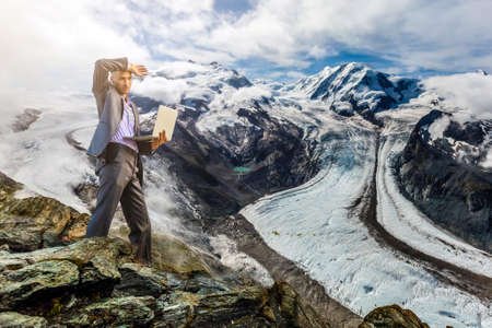 Man working with laptop sitting on the rocky mountain on beautiful scenic clif backgroundの写真素材
