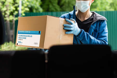 Contactless delivery during COVID-19 pandemic lockdown concept. Courier wearing mask and gloves deliver a parcel with medical equipment and to the customerの写真素材