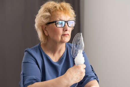 Sick elderly woman making inhalation, medicine is the best medicine. Ill senior woman wearing an oxygen mask and undergoing treatment. Senior woman with an inhalerの写真素材