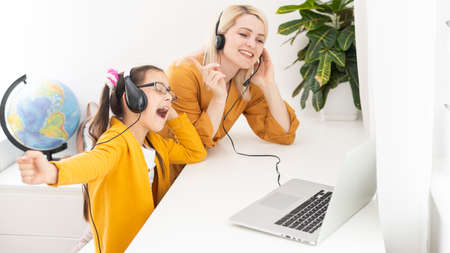 Mother and her girl listening to music on laptop. They sitting in living room. Natural light ambient.の写真素材