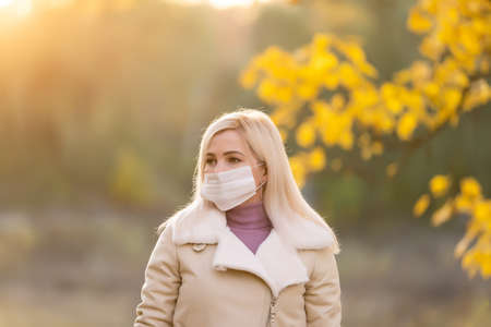 Autumn woman in medical protective face mask walking outdoors, fall season portraitの写真素材