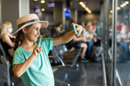 tourism, vacation, childhood and transportation concept - smiling little girl with travel bag, ticket and passport over airport background.の写真素材