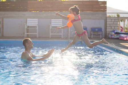 father catches little girl jumping in pool against seaの写真素材