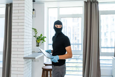 Thief with black balaclava stealing laptop. The burglar commits a crime in Luxury apartmentの写真素材