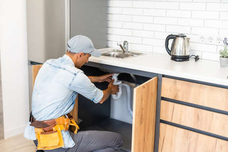 plumber fixes sink siphon by two pipe-wrenches in kitchen.の写真素材