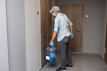Courier in face mask with clipboard and bottles of cooler water in entryway.の写真素材