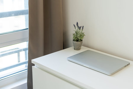 Workspace with laptop closed, on white table with white wall background