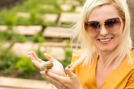 Close-up portrait of a young woman holding snails, taking care of them in the farm for snails growingの写真素材