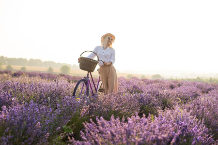 Beautiful young healthy woman with a white dress running joyfully through a lavender field holding a straw hat under the rays of the setting sunの写真素材