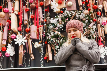 Gorgeous fashionable young blonde woman sitting near the window of the store or coffeehouse, dreaming, praying for a miracle before Christmas. cold winter day.の写真素材
