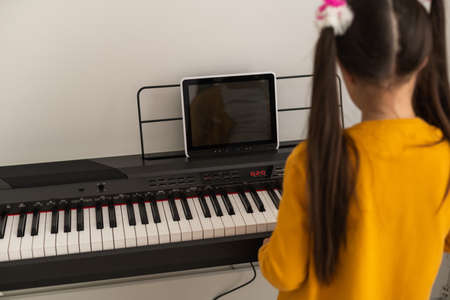 Cute serious little girl plays on the electric piano on whiteの写真素材