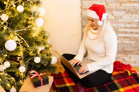 woman with laptop on the background of a Christmas tree accepts online congratulations merry christmasの写真素材