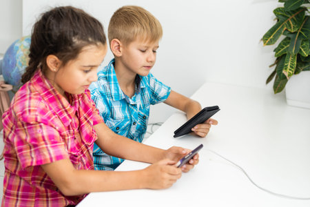 boy playing with smartphone next to his sister in the room at home.