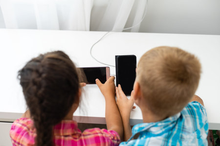 Two preschool children boy and girl sit together and play with smartphone