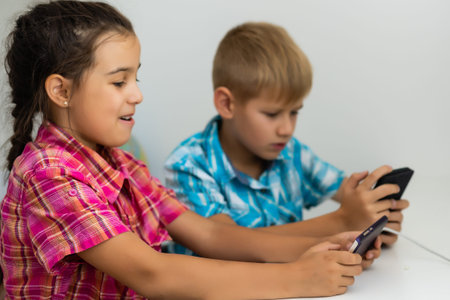 boy playing with smartphone next to his sister in the room at home.