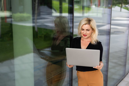 Image of young beautiful joyful woman smiling while working with laptop from outside
