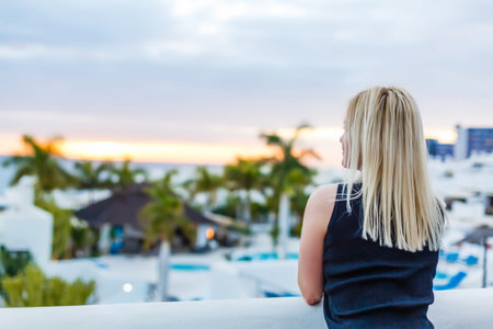 Woman relaxing by the pool in a luxurious beachfront hotel resort at sunset enjoying perfect beach...