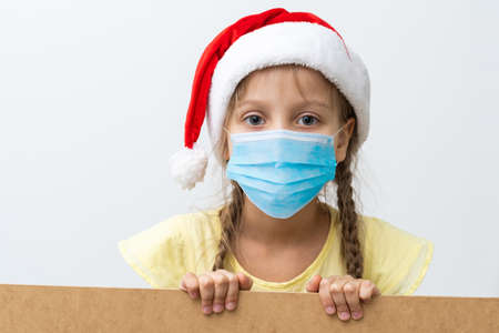 Portrait of a beautiful little girl wearing Santa hat, medical mask, isolated on white background, copy space. celebrating happy New Year. Child safety social distanceの写真素材