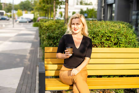 Cheerful fashionable blonde holding coffee outdoorsの写真素材