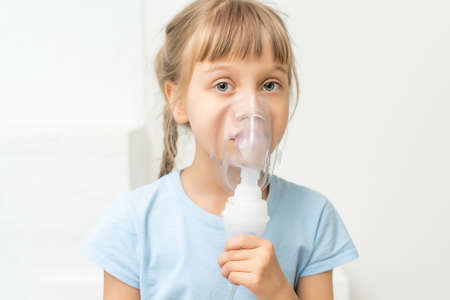 sick little girl makes inhalation over grey background with copy space. Girl making inhalation with nebulizer at home. child asthma inhaler inhalation nebulizer steam sick coughの写真素材