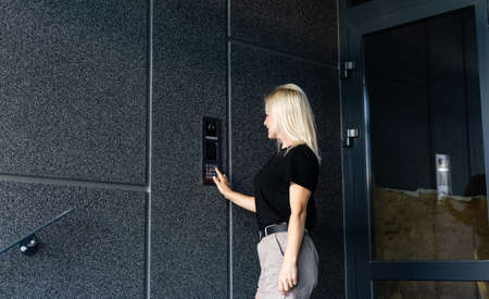 Happy woman ringing on doorbell at building entrance. Using intercom.の写真素材