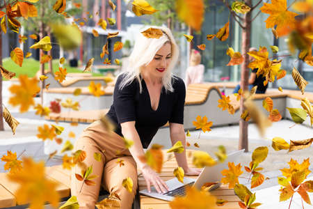 Cute woman with laptop in the autumn parkの写真素材