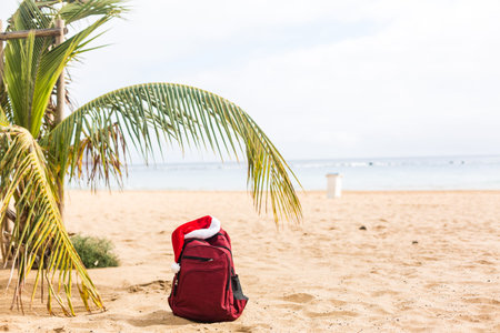 Santa Claus hat on backpack standing on sand beach. Christmas and New Year celebration. Nobody.の写真素材