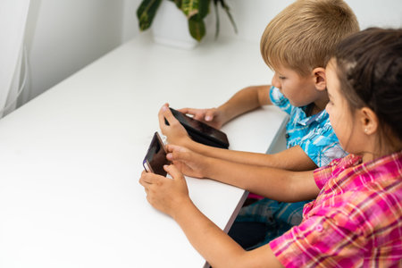 boy playing with smartphone next to his sister in the room at home.