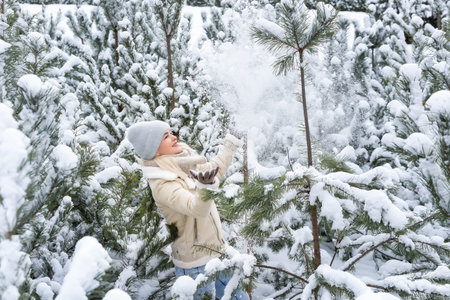 A girl in white clothes stands near a pine tree in the snow.