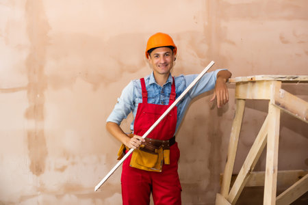 repair, building, construction, people and maintenance concept - smiling man with helmet over wall...