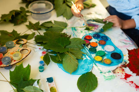 Cute schoolgirl with scissors cutting dry oak leaf while helping her teacher with decorations for holiday at lessonの写真素材