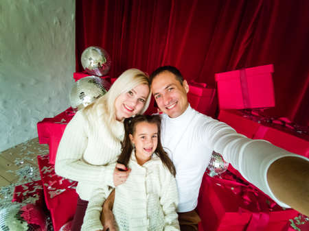 family, holidays, technology and people - smiling mother, father and little girl making selfie with camera over living room and christmas tree backgroundの写真素材