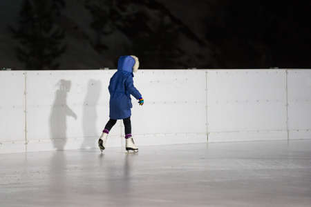 Cute little girl ice skating on a rink in the city centerの写真素材