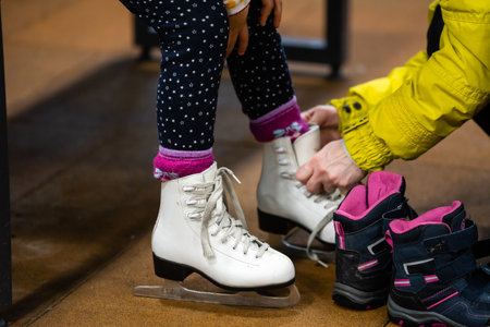 Family in a winter park. Mother with daughter in a ice arena. Mom puts her daughter in skatesの写真素材
