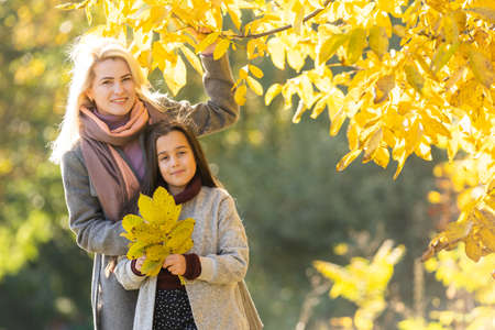 Little girl and her mother enjoy sunny weather in the autumn parkの写真素材