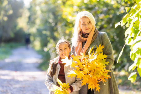 Little girl and her mother enjoy sunny weather in the autumn park