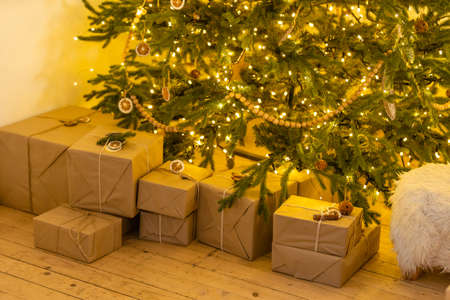christmas gifts in craft paper with yellow, pink and white ribbons, pine branches and a garlandの写真素材