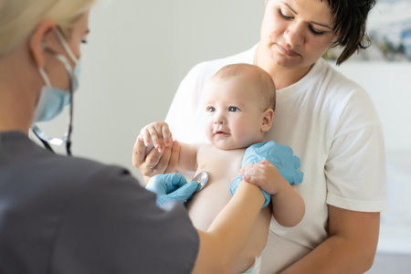 Female doctor examining little smiling baby girl, held by motherの写真素材