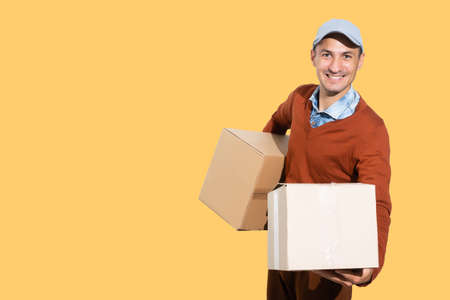 Cheerful delivery man. Happy young courier holding a cardboard box and smiling while standing against orange backgroundの写真素材
