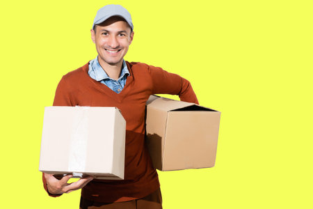 Cheerful delivery man. Happy young courier holding a cardboard box and smiling while standing against light green backgroundの写真素材