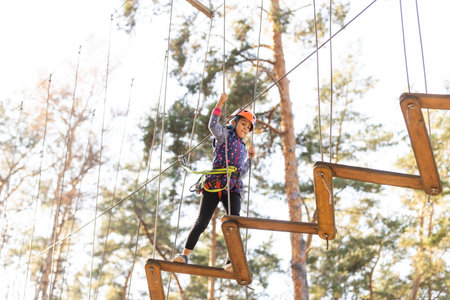 Child in forest adventure park. Kids climb on high rope trail. Agility and climbing outdoor amusement center for children. Little girl playing outdoors. School yard playground with rope way.の写真素材