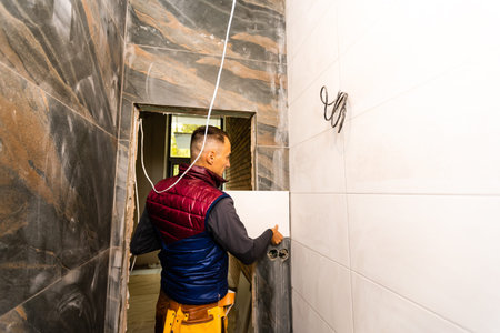 Laying Ceramic Tiles. Tiler placing ceramic wall tile in position over adhesive