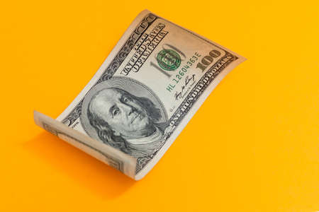 Single Hundred Dollar Bill Curled on yellowの写真素材