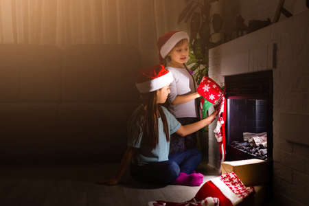Little kids opening presents next to the fireplace in a cozy home celebrating Christmasの写真素材