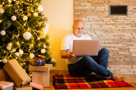 christmas, holidays and people concept - happy smiling senior elderly man sitting with laptop online at christmas at homeの写真素材