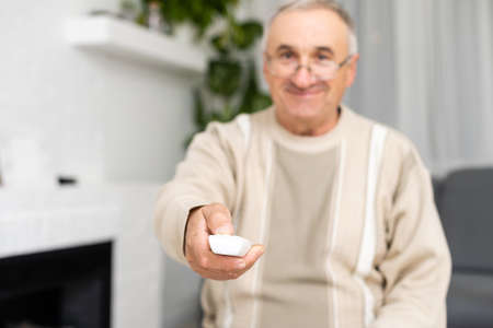 Portrait of an old man using remote control and watching tv. Indoors.の写真素材