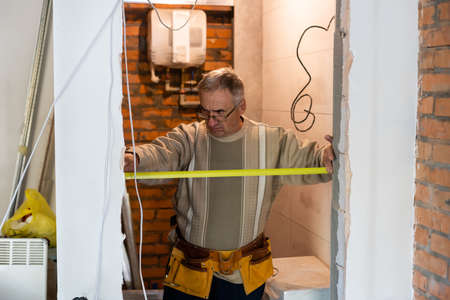 Grey haired handyman measuring wallの写真素材