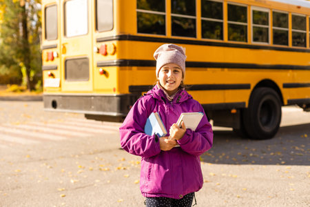 Little girl standing by a big school bus with her books.